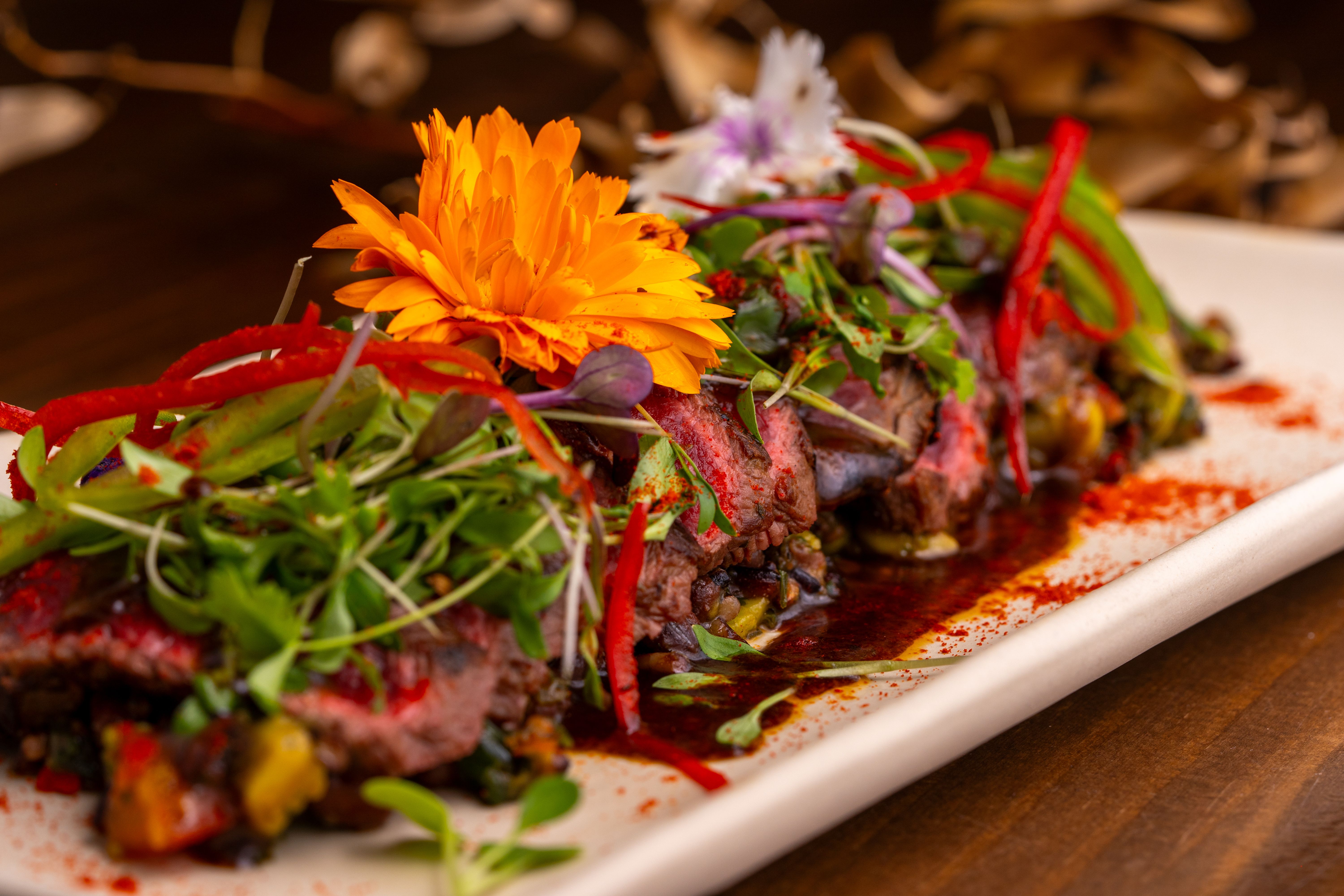 Gourmet steak dish with colorful edible flowers and fresh herbs, demonstrating appetizing contrast and presentation.