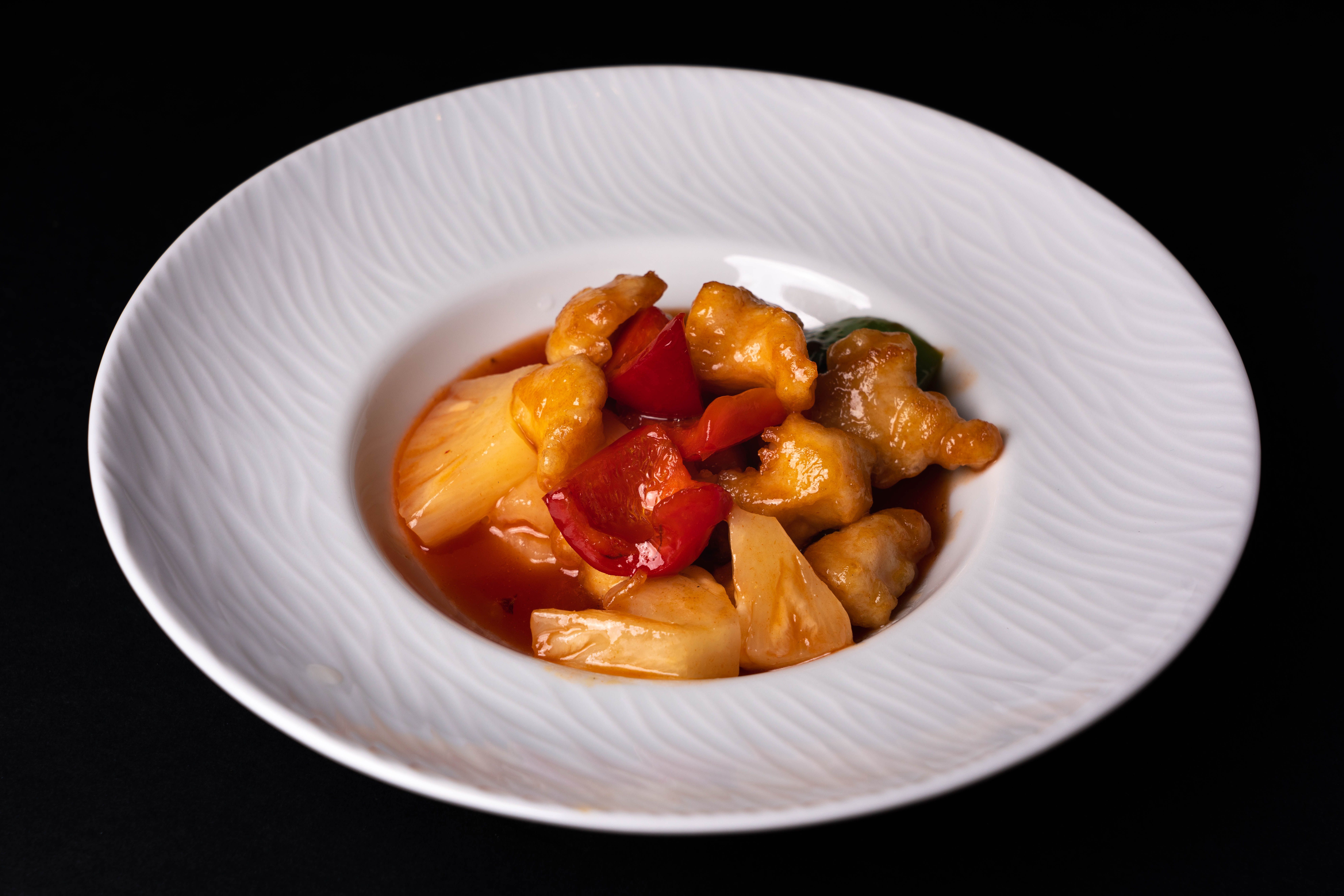 Sweet and sour chicken with vivid red and orange bell peppers on a plate, showing how warm food colors attract attention.